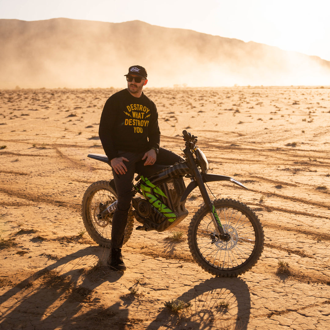 A guy is resting on a rawrr mantis model in a desert.